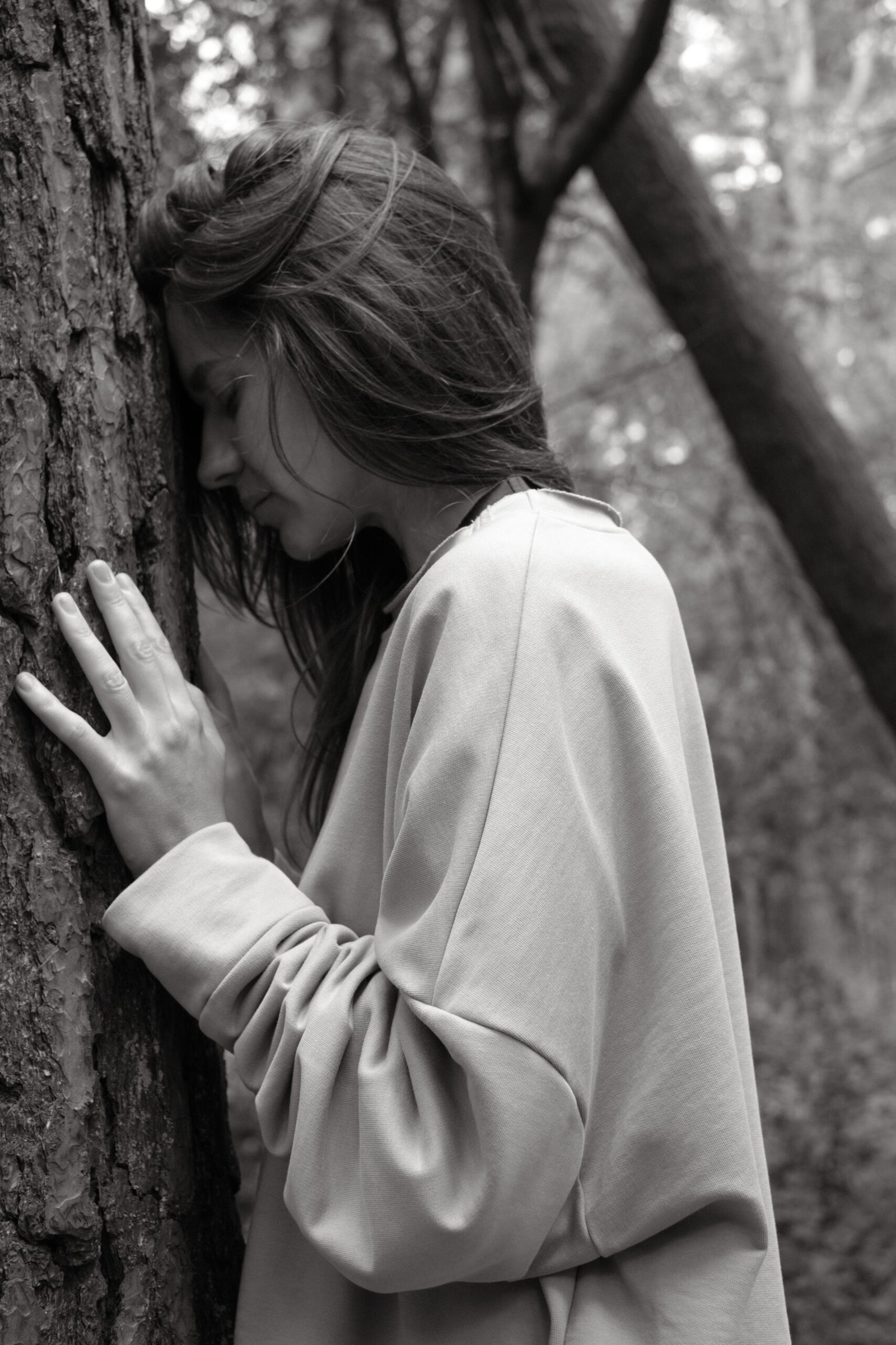 Model in MATSU oversized sweatshirt leaning against a pine tree in a quiet forest
