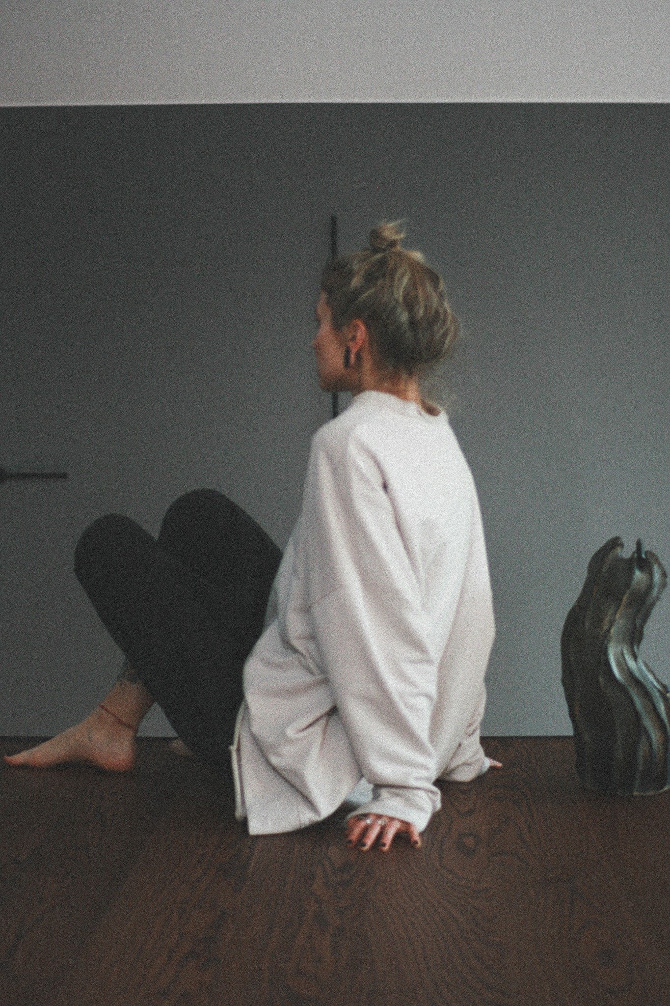 Unisex sweatshirt showcased in a neutral pose with a focus on the relaxed and oversized fit, featuring dropped shoulders. The garment has a loose-fitting raw-edge neckline, straight hem and cuffs, with a slightly longer hem at the back. The model stands against a plain grey background that highlights the sweatshirt's design and comfortable silhouette.